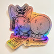 Rainbow holographic art sticker of a hairless cat with a headwrap hunched over a tarot card of The High Priestess surrounded in crystals and melting candles 