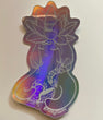 Art sticker on rainbow holographic material of a cartoon ambiguous figure with hair tied in a side braid washing a bowl with a sponge with a content and meditative expression. On their forehead is an infinity figure-eight symbol and on the top of their head is a blooming lotus flower